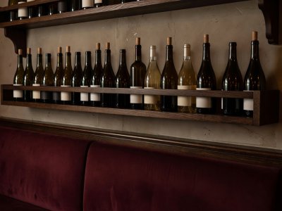 Row of natural and regional wine bottles lined along a dark oak bistro shelf above banquette seating